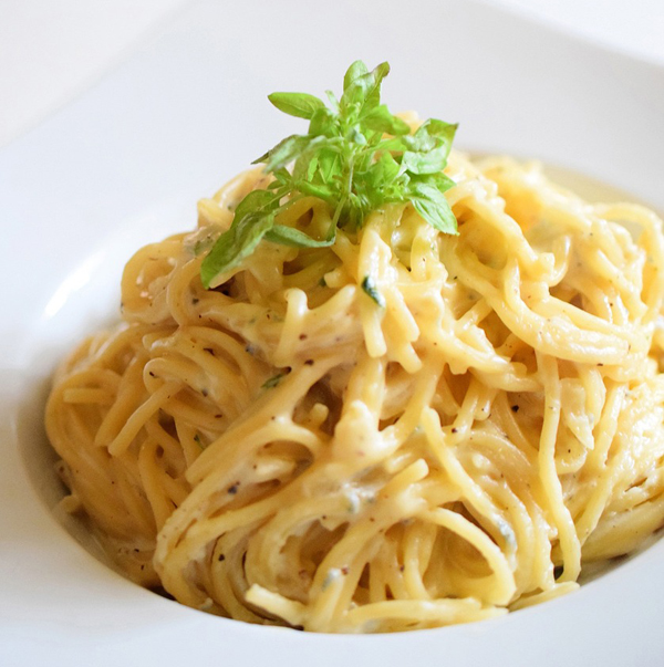 white sauced spaghetti twirled onto a plate with basil sprig on top