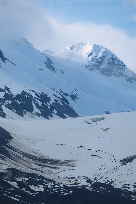 Light on mountain peak with snow covered sides and swirls of black in Alaska