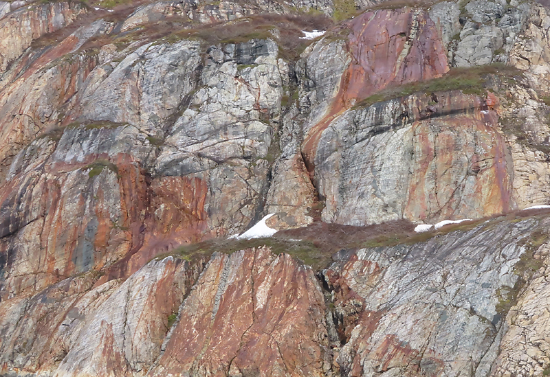 grey rock cliff with natural iron painted streaks and green patches of grass in Alaska