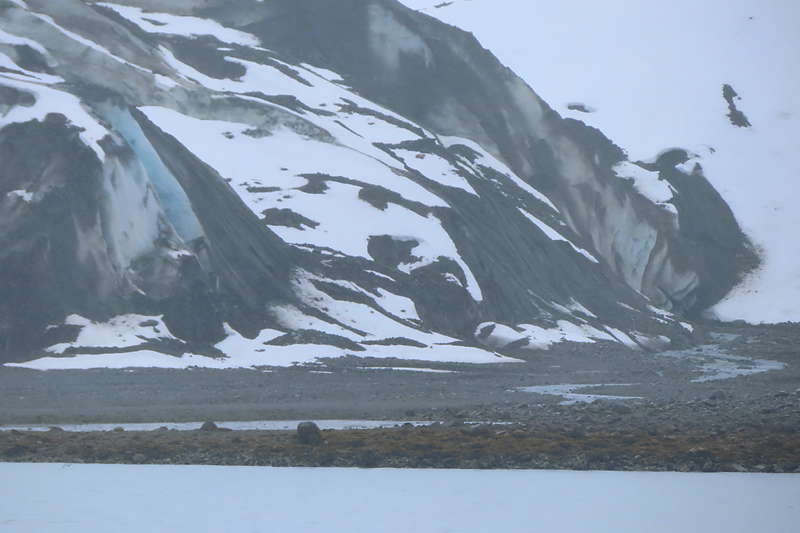 snow covered glacier front with rocky shore and light blue water in Alaska