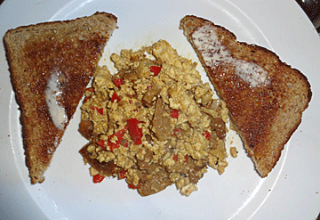 yellow tofu scramble with mushrooms and red peppers on plate with 2 slices of toast with butter